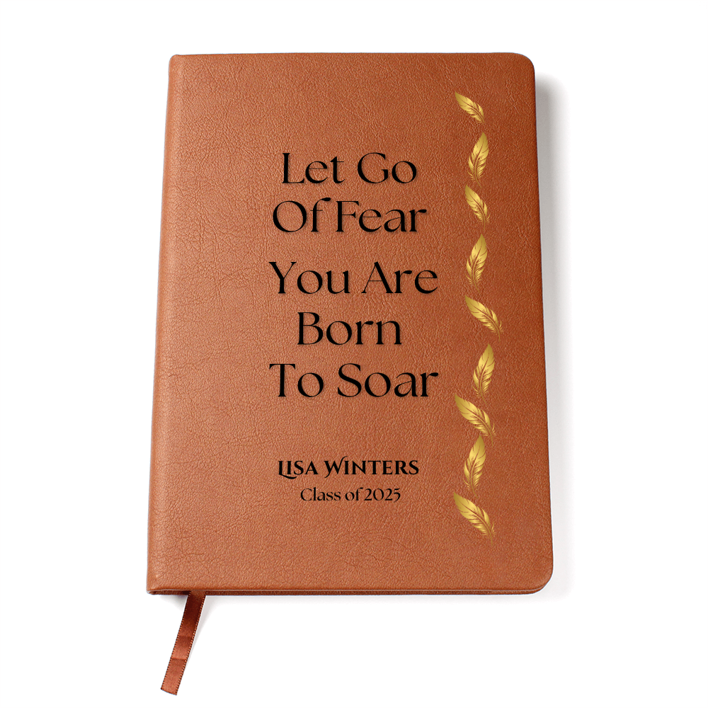 Personalized brown leather graduation journal on white desk with golden feather design and quote "Let Go of Fear, You Are Born to Soar" – includes name and class year.